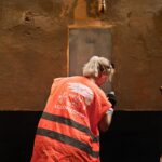 3 persone di spalle con una pettorina fluorescente ripuliscono un muro vandalizzato