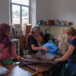 Persone che piegano dei vestiti attorno a un tavolo.