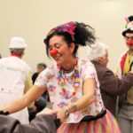 una clown dottore sorridente balla con una persona anziana in una Rsa