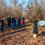 un gruppo di persone davanti a un pannello escursionistico nel bosco