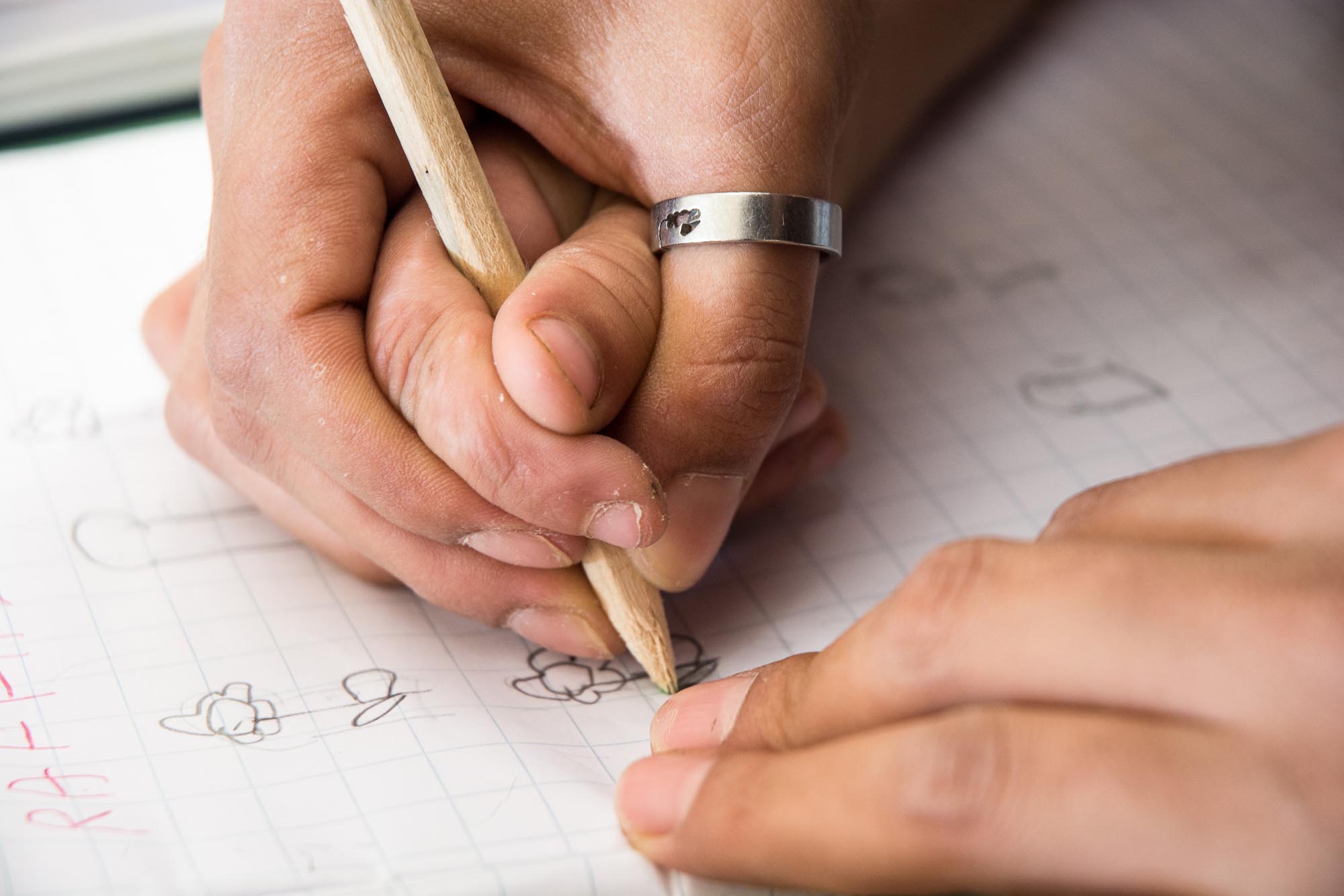 Primo piano di mani che impugnano una matita e scrivono su un foglio a quadretti.