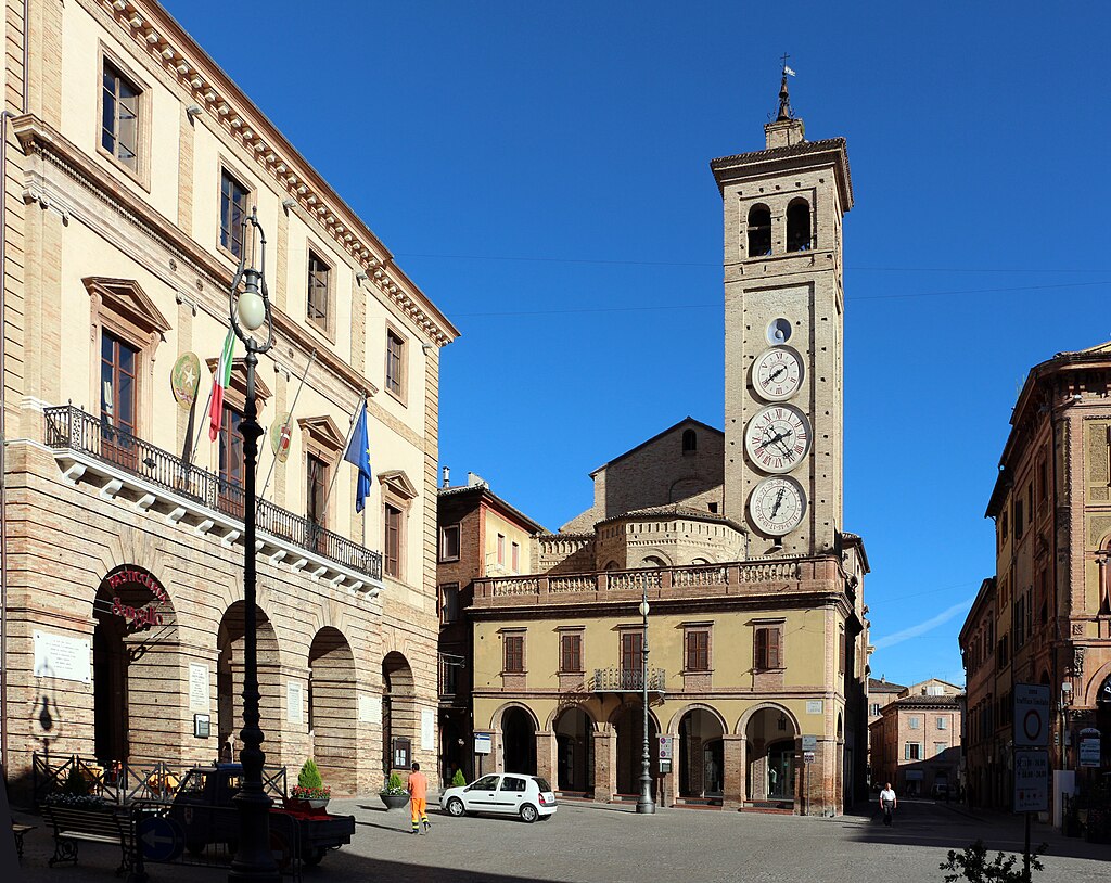 una piazza con torre dell'orologio e palazzo del comune con archi