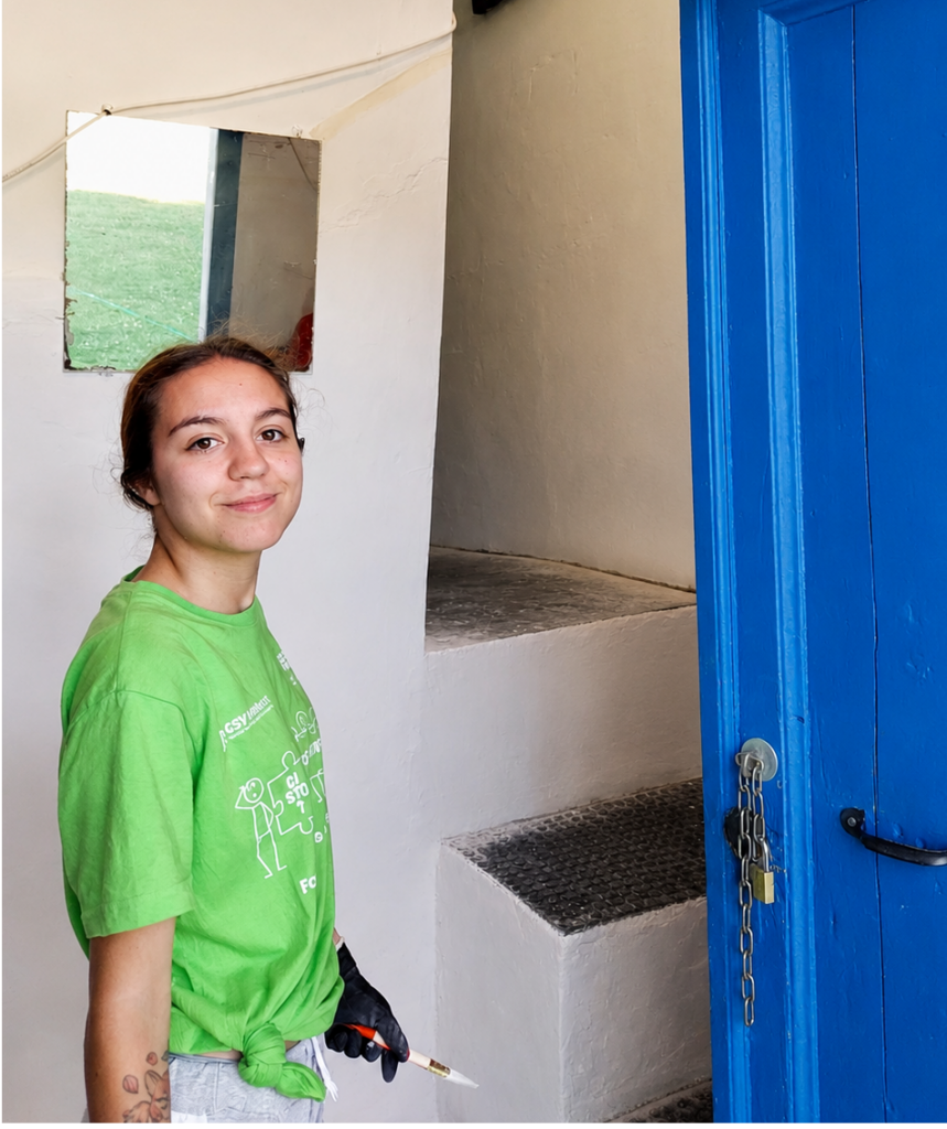Asya Brescini con un pennello in mano davanti a una porta di legno blu