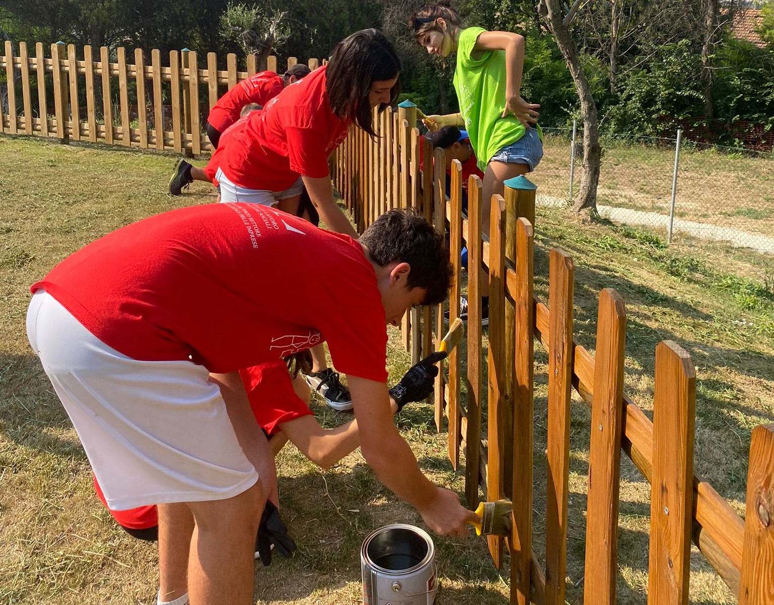 ragazzi con le magliette rosse verniciano una staccionata in un parco