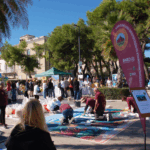 lungomare con palme, stand e persone che assistono alla creazione di un tappeto di fiori