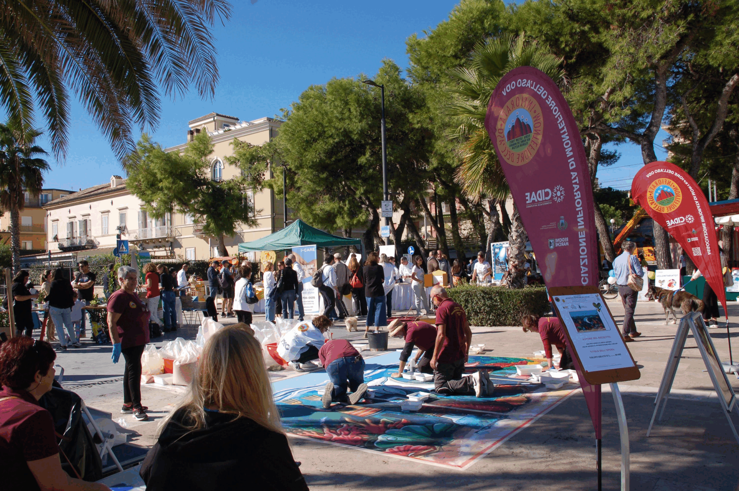 lungomare con palme, stand e persone che assistono alla creazione di un tappeto di fiori