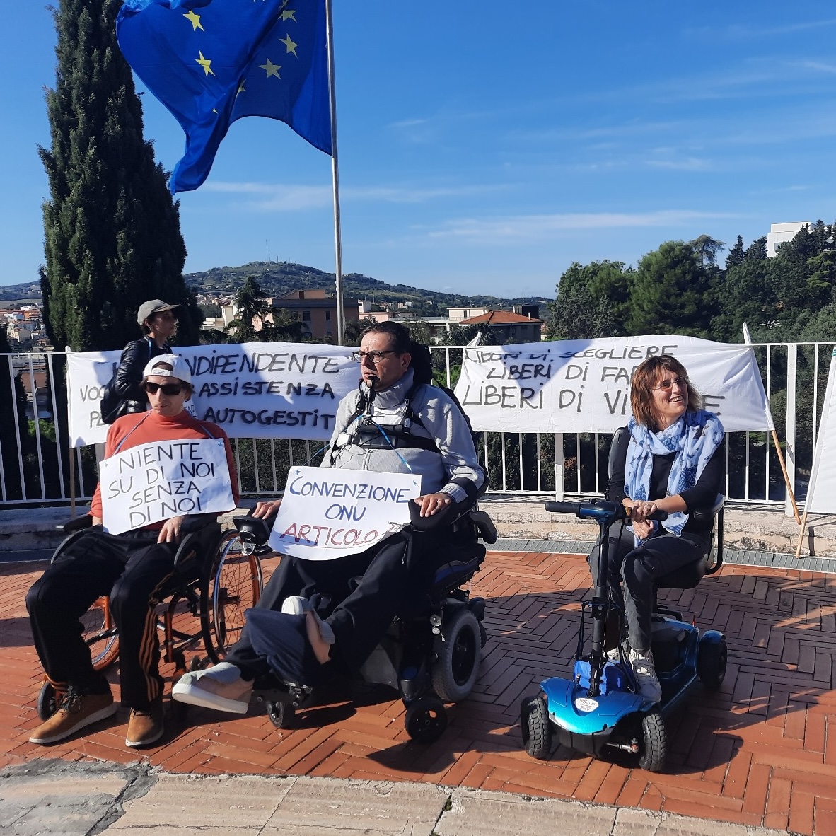 Tre persone su carrozzina ad una manifestazione.