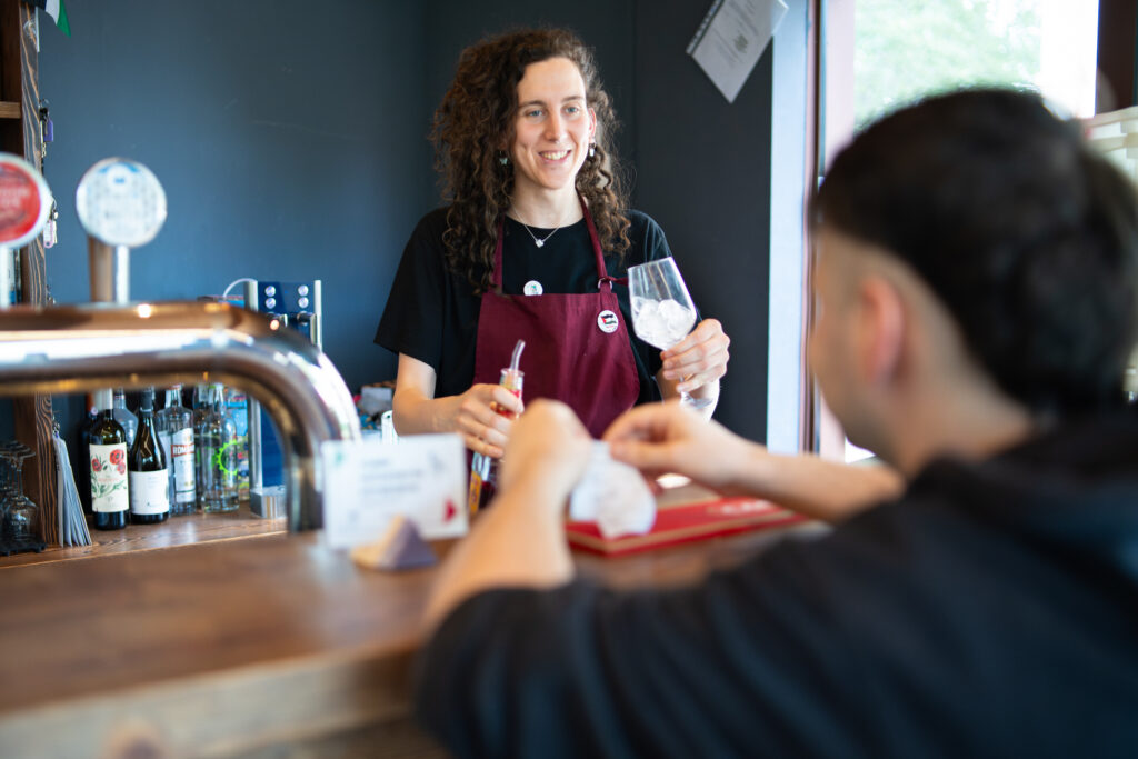 Lara dietro al bancone di Ask, con un bicchiere in mano, mentre prepara un cocktail 