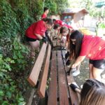squadra di giovani con indosso la stessa t shirt rossa mentre puliscono delle panchine in un parco