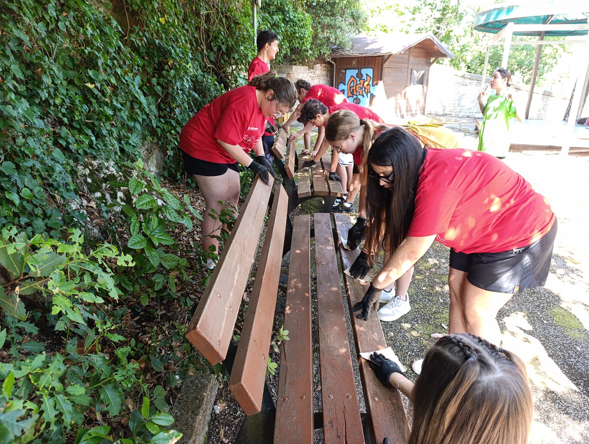 squadra di giovani con indosso la stessa t shirt rossa mentre puliscono delle panchine in un parco