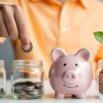 una persona inserisce una moneta nel secondo di quattro vasetti/salvadanai in fila davanti a sè