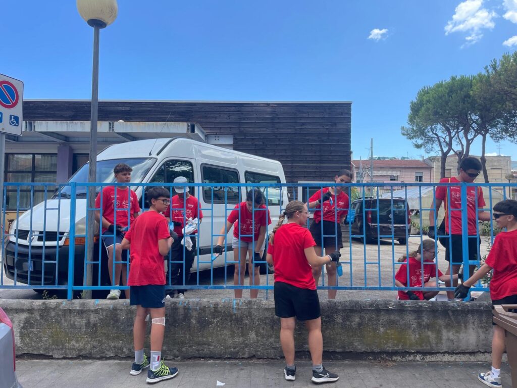 un gruppo di giovani con la tshirt rossa mentre vernicia d'azzurro una ringhiera