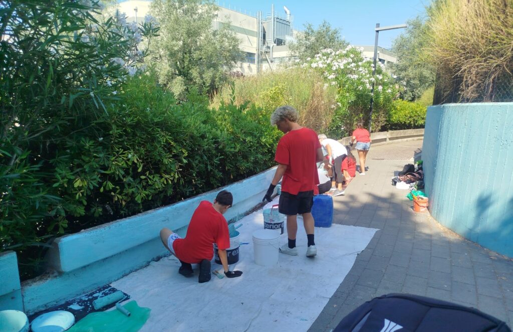 giovani con una tshirt rossa mentre verniciano d'azzurro un muretto