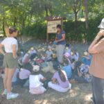 Bambini seduti attorno a un adulto in un luogo tra gli alberi.