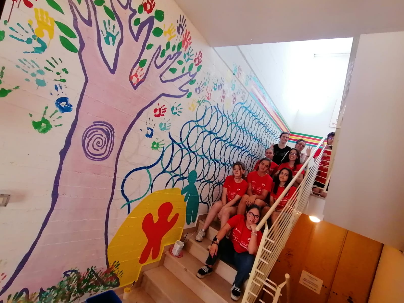 una squadra di giovani partecipanti al progetto vicino a una parete dipintacon murales
