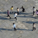 dieci bambini giocano a rincorrersi in una piazza