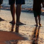 le gambe di tre persone in riva al mare, tra cui un bambino