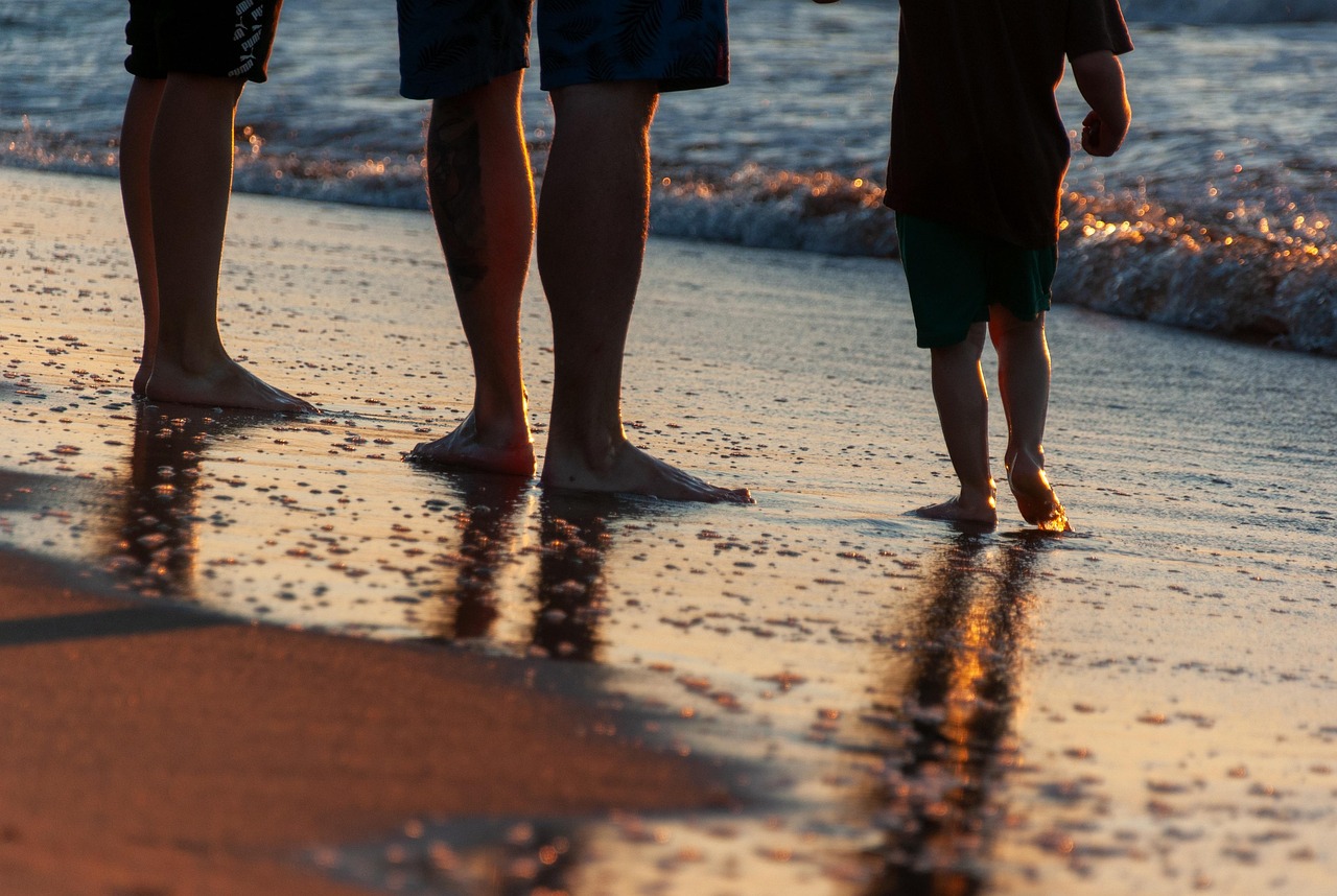 le gambe di tre persone in riva al mare, tra cui un bambino