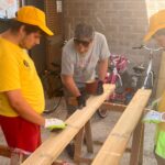 Tre persone lavorano a delle assi di legno