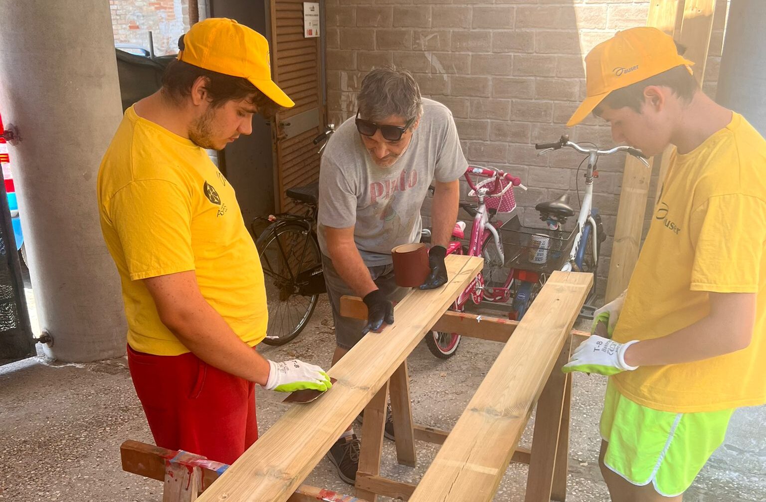 Tre persone lavorano a delle assi di legno