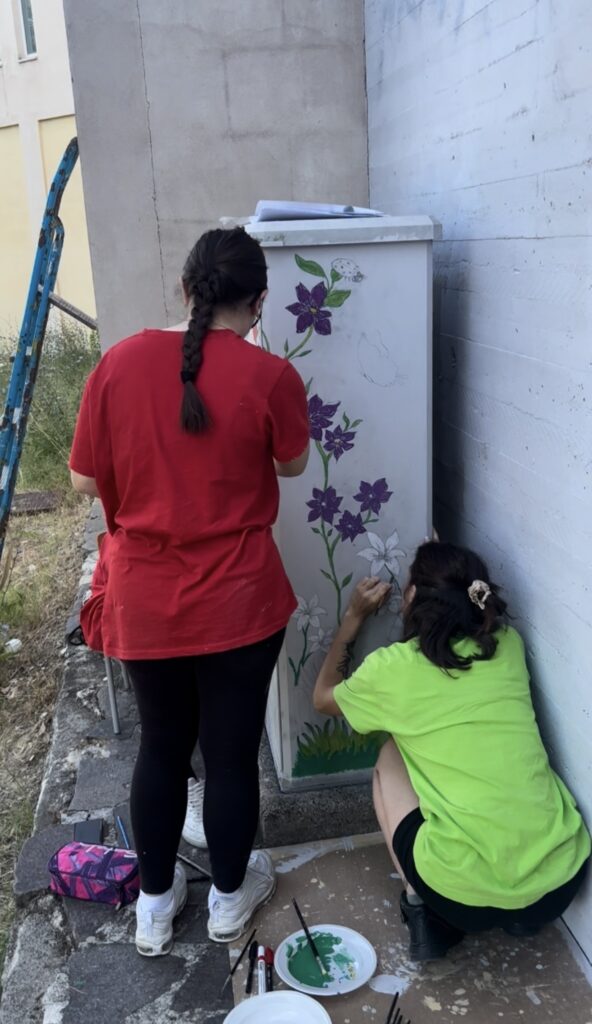 Asya Brescini e un'altra ragazza, di schiena, dipingono dei fiori su una parete