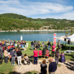 gruppo di persone in un prato a bordo lago partecipa a una presentazione con dimostrazione di joelette