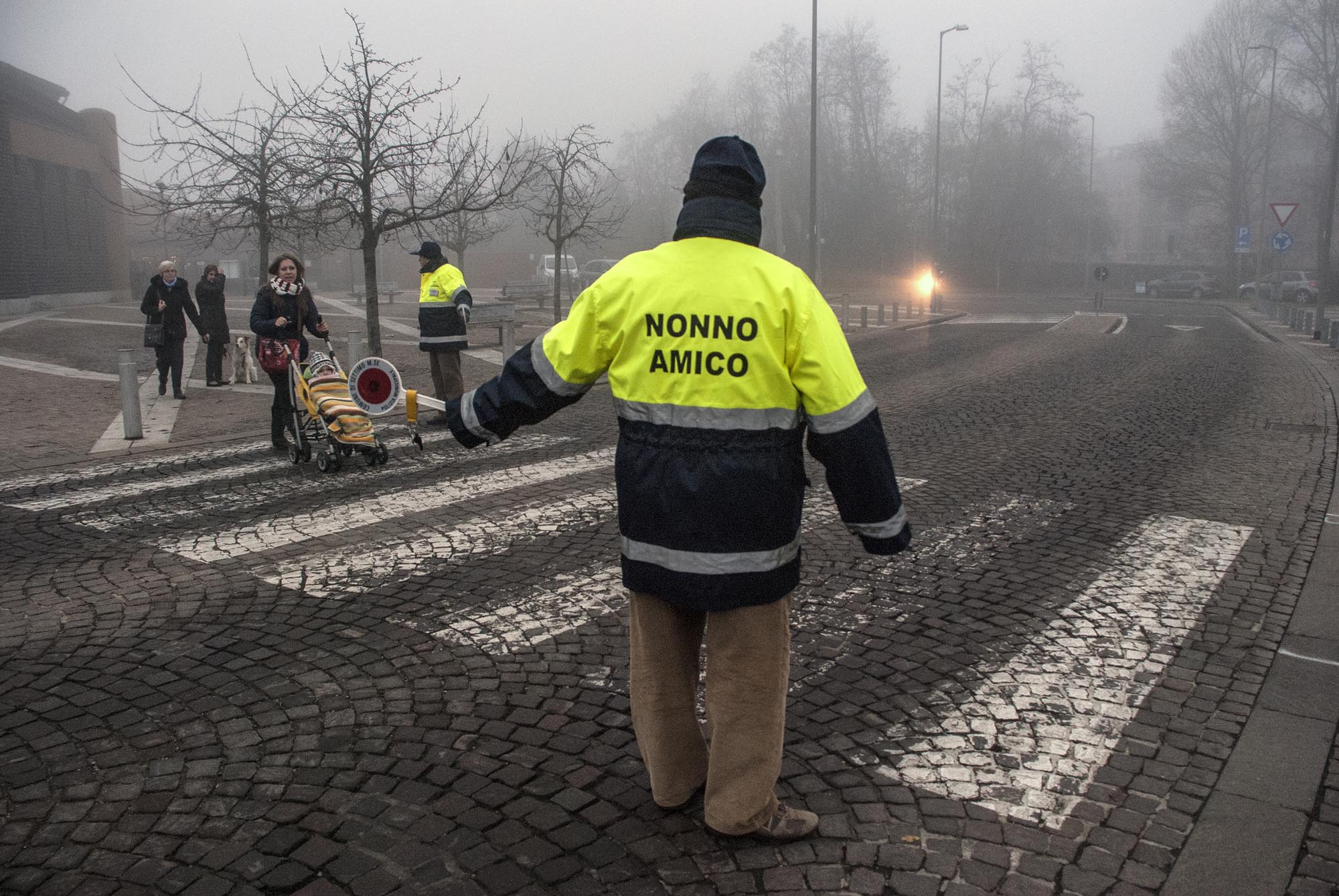 un volontario "nonno amico" aiuta dei pedoni ad attraversare la strada