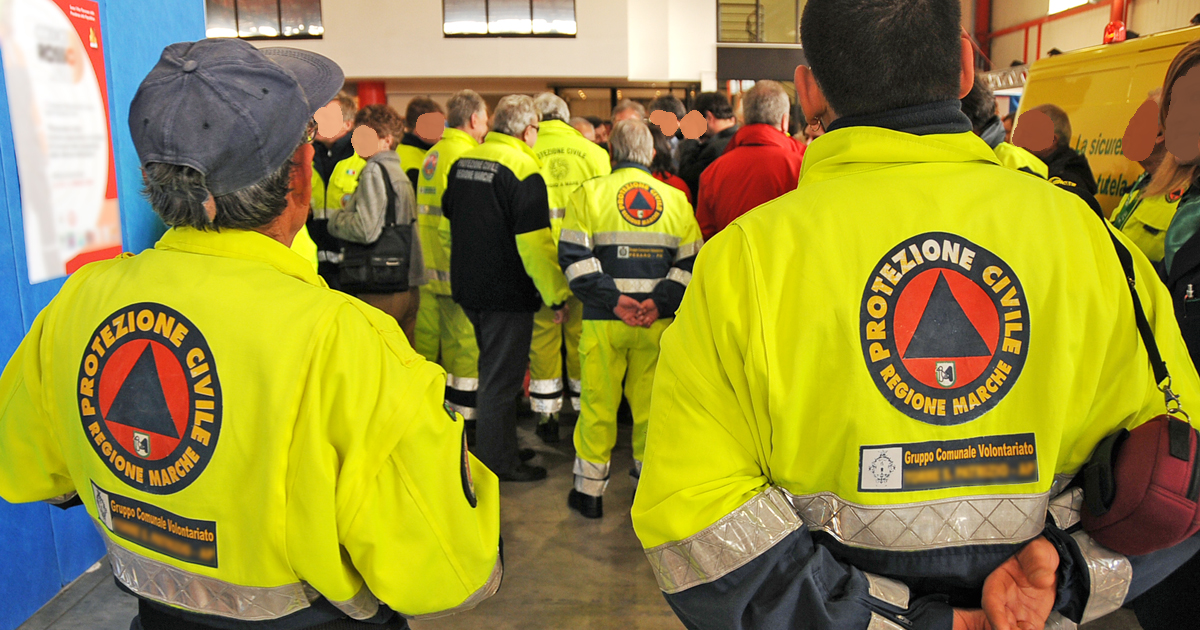 Un gruppo di volontari della protezione civile Marche in divisa, ritratti di spalle