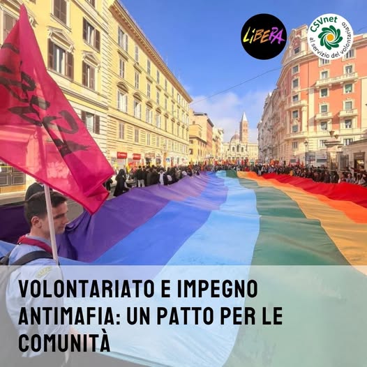 una bandiera dell'ass. Libera accanto a una lunga bandiera della pace tenuta ai lati dai manifestanti di un corteo