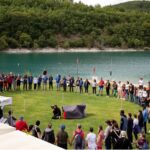 numerose persone per mano formano un grande cerchio vicino a un lago