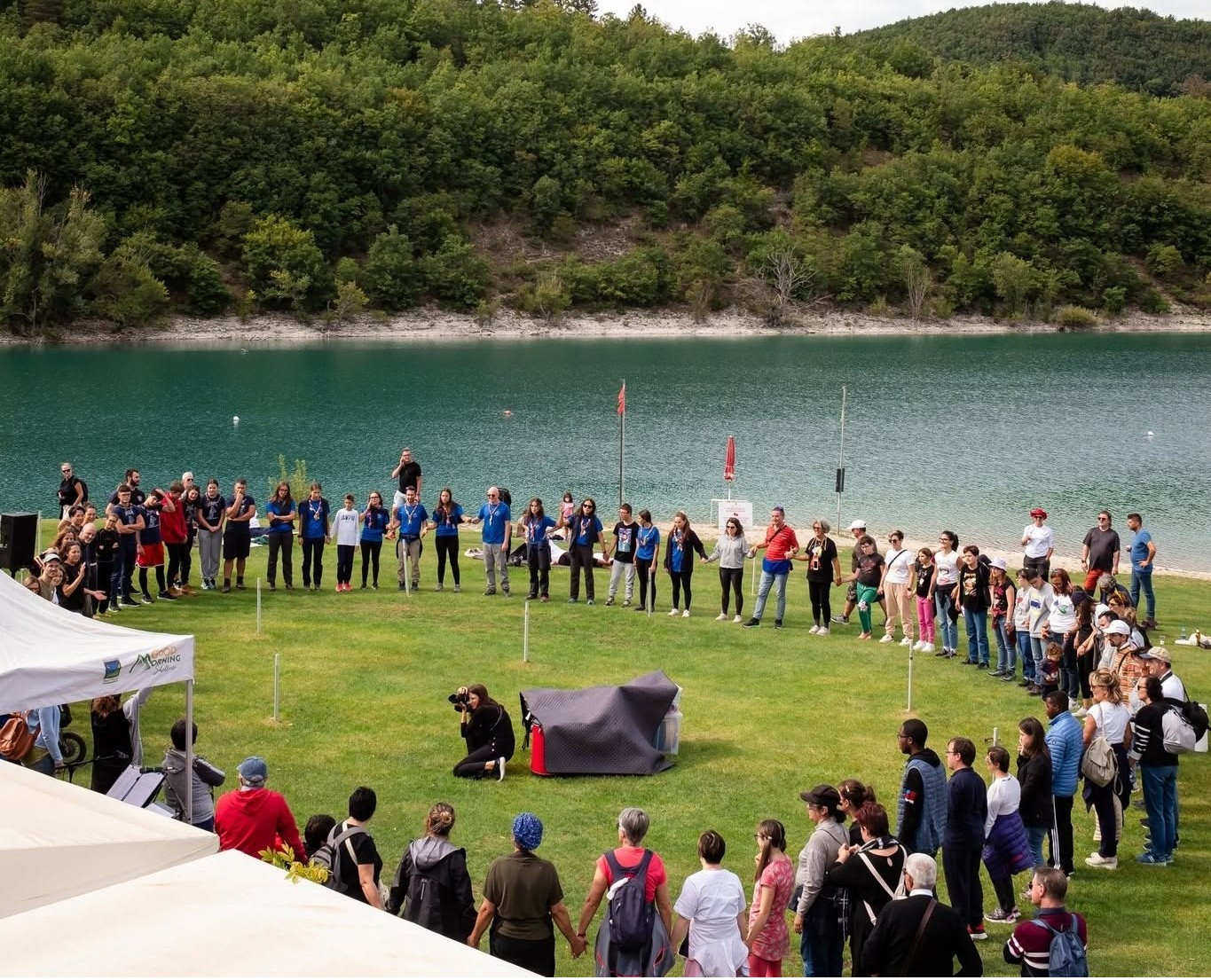 numerose persone per mano formano un grande cerchio vicino a un lago