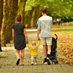 due adulti a passeggio tengono per mano un bambino e spingono un passeggino