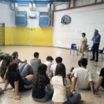 bambini seduti in una palestra davanti a due adulti