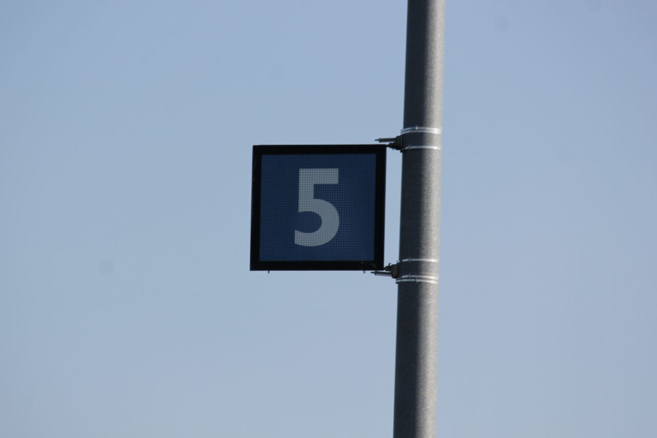 Close-up of metal pole with number 5 sign against a clear blue sky.