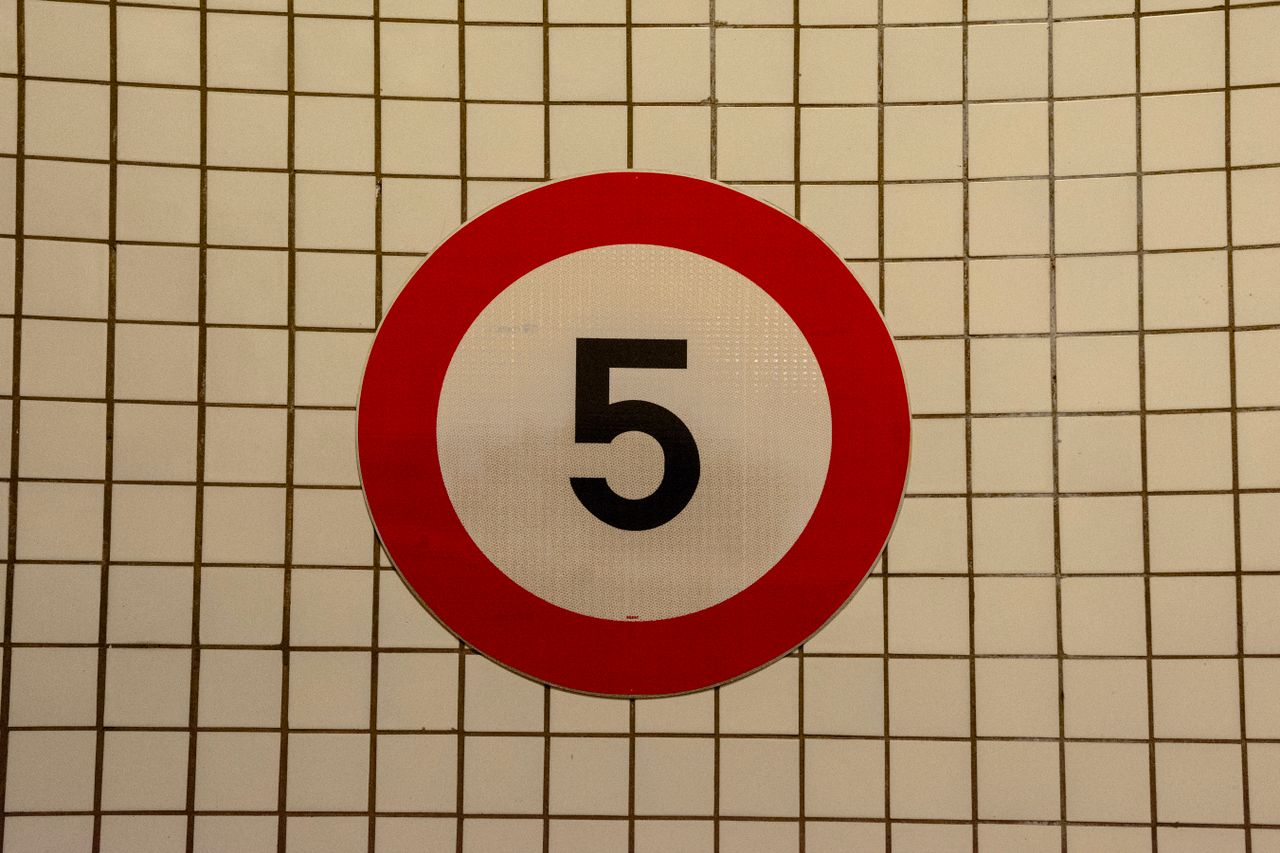 Close-up of a speed limit sign with the number 5 against a tiled wall background.
