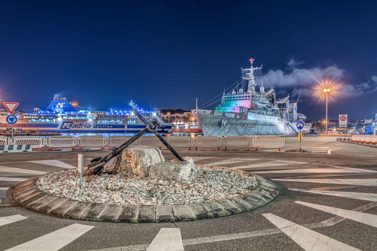 Captivating view of Ancona's port at night featuring ships and a prominent anchor monument.