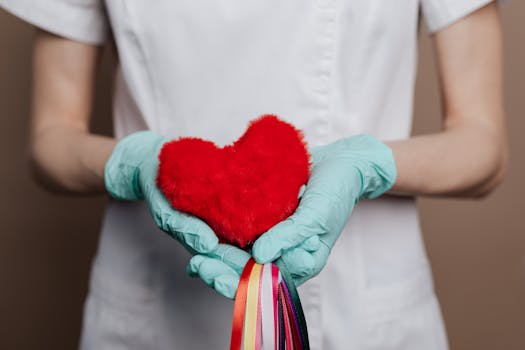 A nurse in gloves holds a red heart with rainbow strings, symbolizing love and healthcare.