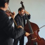 Two musicians performing with a double bass and violin in an intimate indoor setting.