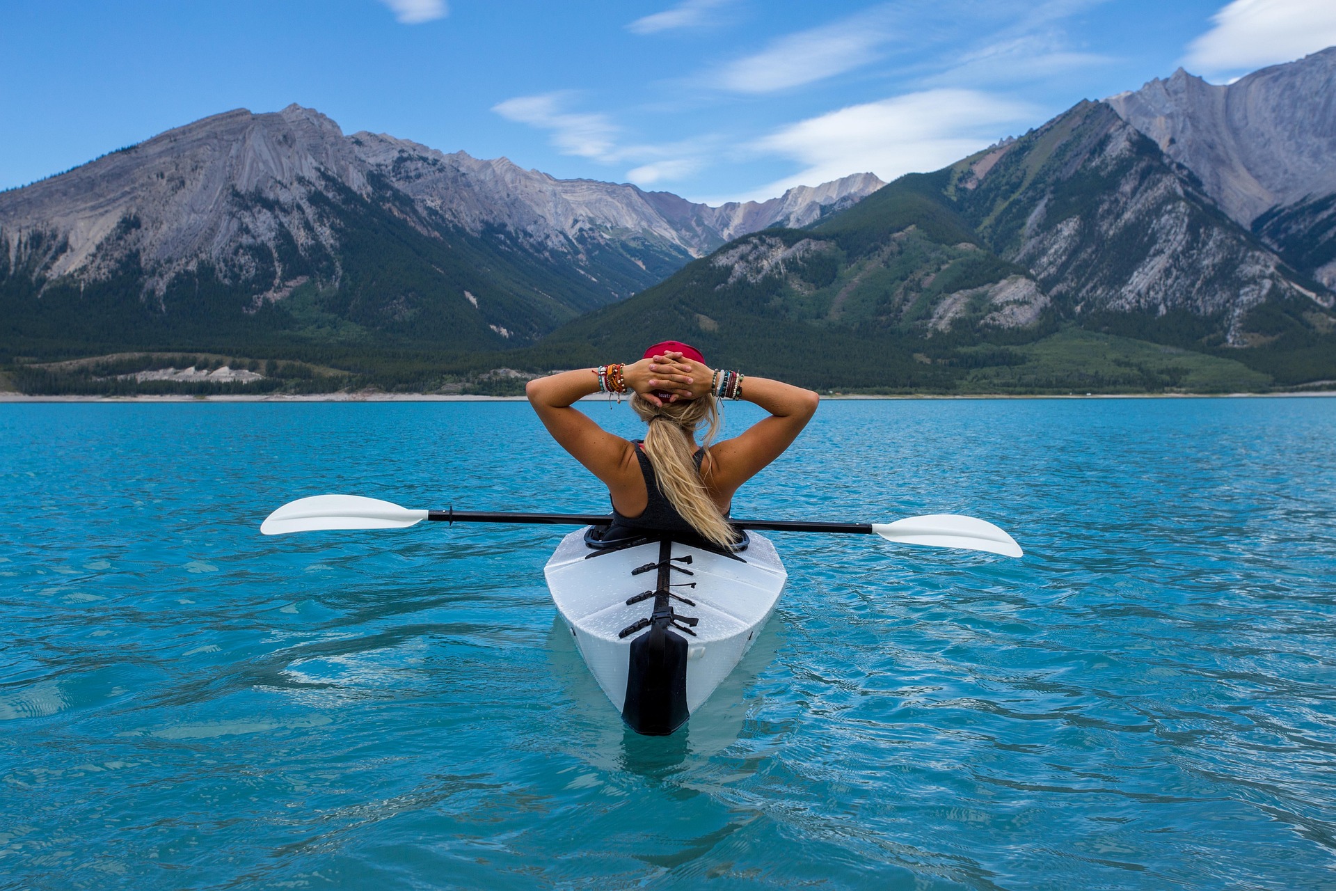 una donna di spalle in un kayak in acqua guarda le montagne all'orizzonte