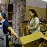 una suora coordina un gruppo di volontari che spostano pacchi alimentari