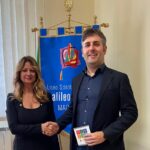 stretta di mano tra la preside del Liceo e il presidente del CSV di fronte allo stendardo della scuola