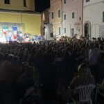 una piazza piena di persone che assistono a uno spettacolo teatrale
