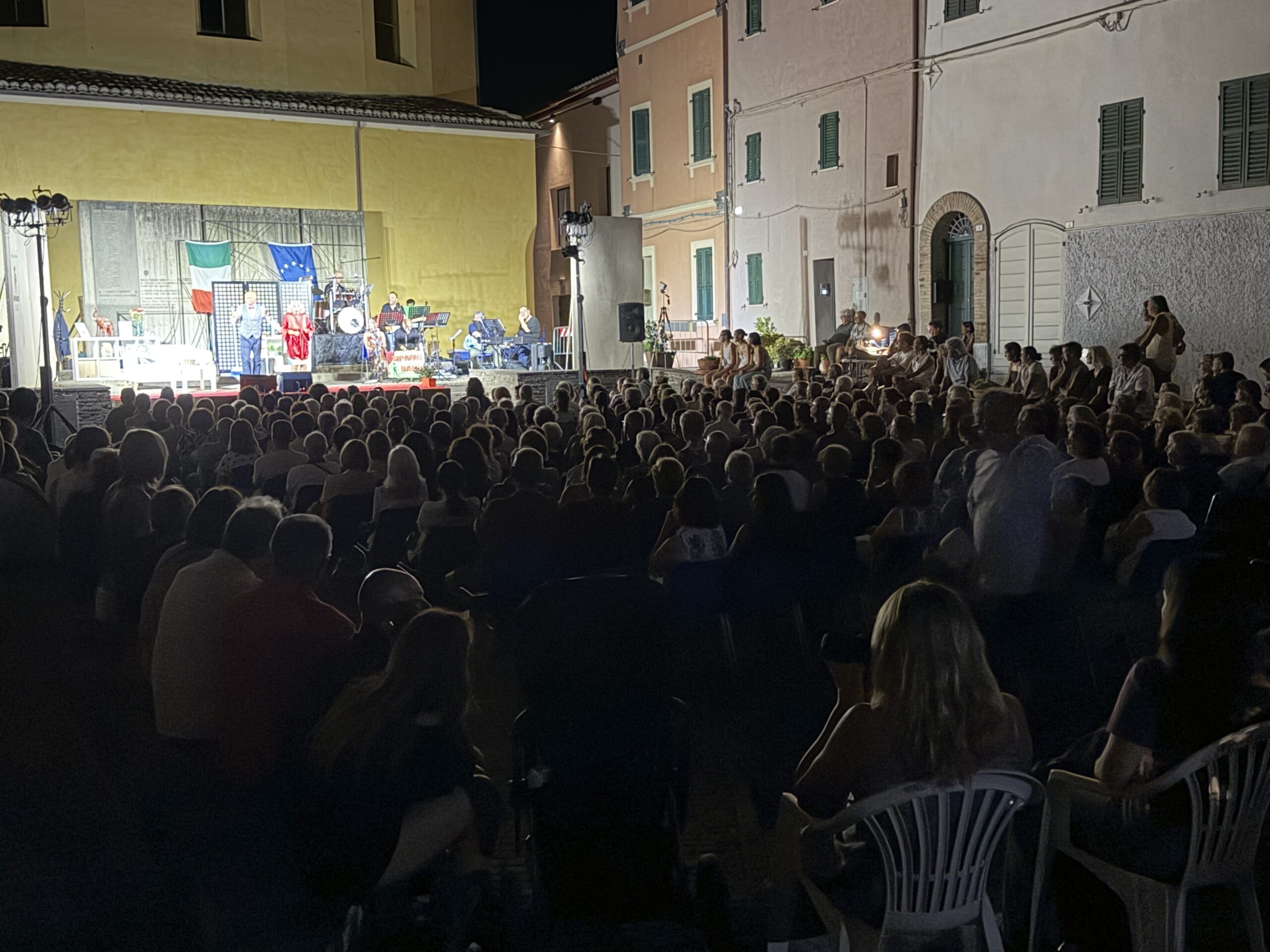 una piazza piena di persone che assistono a uno spettacolo teatrale