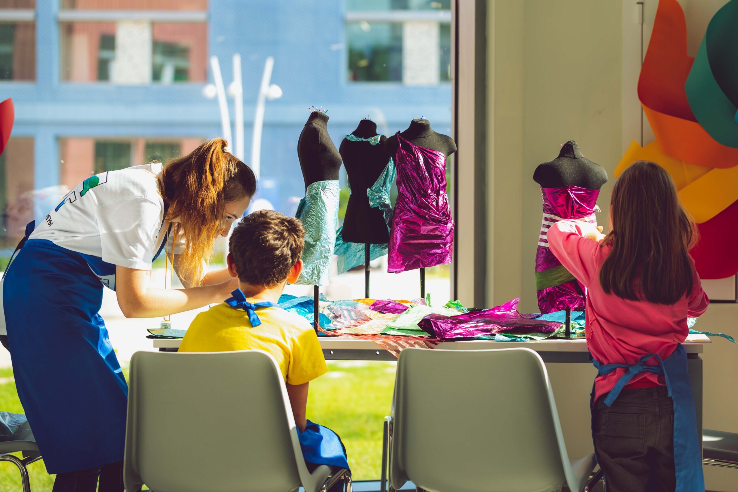 una educatrice insegna a un bambino come usare carta lucida per modellare un abito